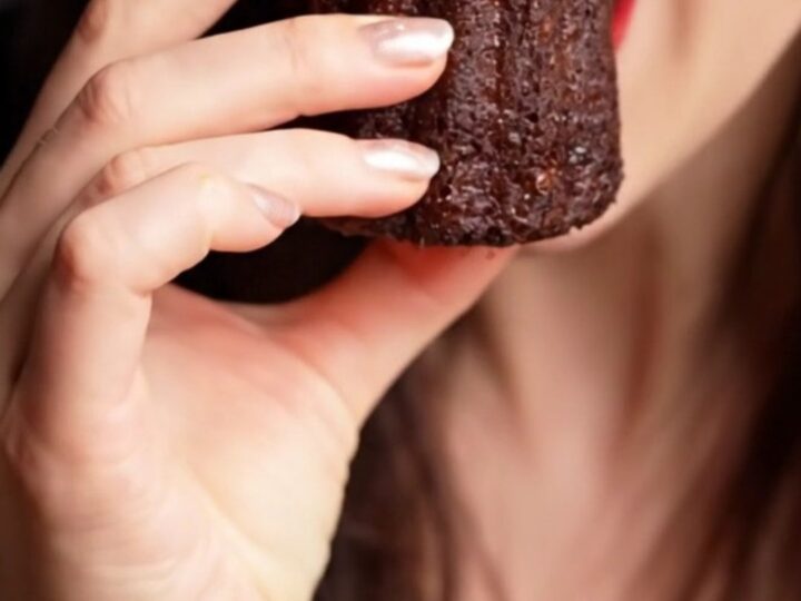 A close-up of a perfectly baked French Canelé with a dark, mahogany-colored, fluted exterior.