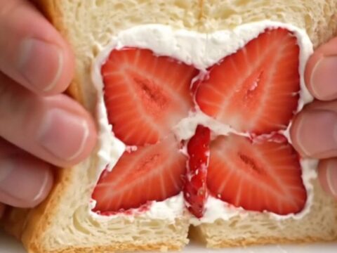 A close-up of a Japanese strawberry sando cut diagonally to reveal a beautiful strawberry flower pattern in thick cream.