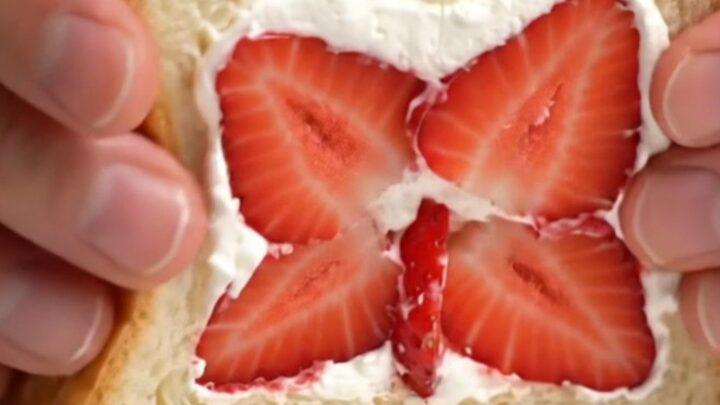 A close-up of a Japanese strawberry sando cut diagonally to reveal a beautiful strawberry flower pattern in thick cream.