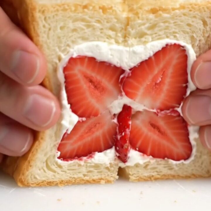 A close-up of a Japanese strawberry sando cut diagonally to reveal a beautiful strawberry flower pattern in thick cream.