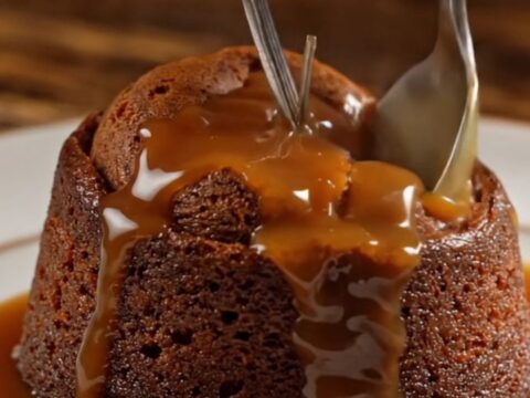 A warm sticky toffee pudding on a dark oak table, topped with a dollop of clotted cream.