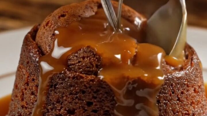 A warm sticky toffee pudding on a dark oak table, topped with a dollop of clotted cream.
