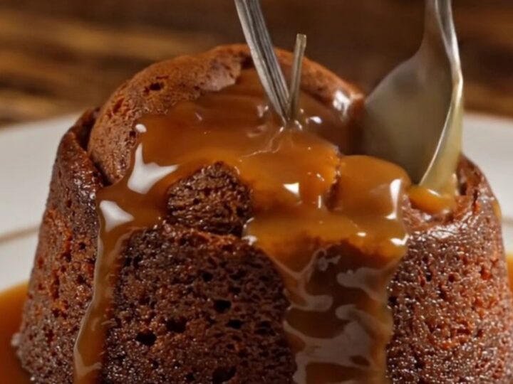 A warm sticky toffee pudding on a dark oak table, topped with a dollop of clotted cream.