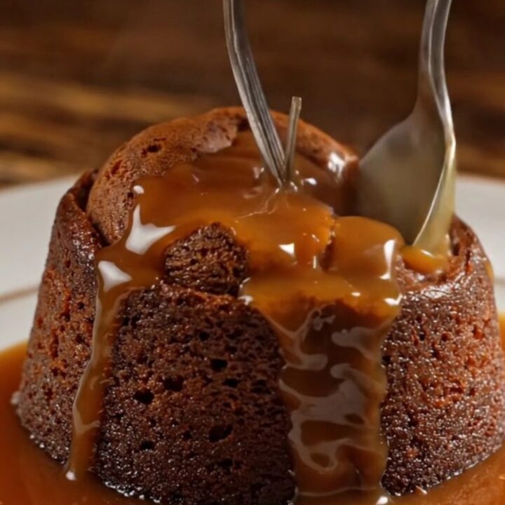A warm sticky toffee pudding on a dark oak table, topped with a dollop of clotted cream.