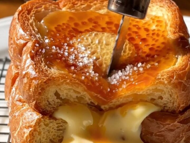 A close-up of a spoon shattering the caramelized sugar crust on a thick slice of stuffed brioche French toast.