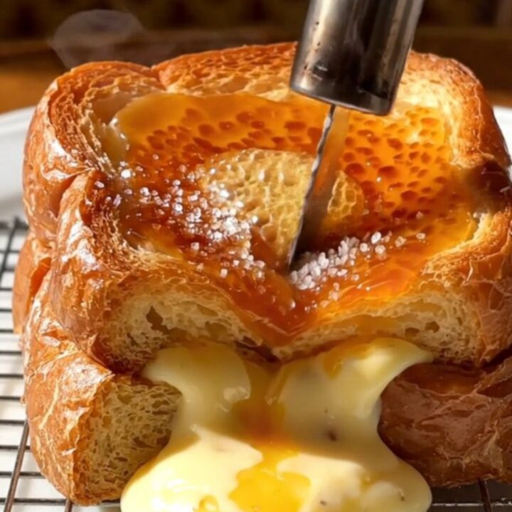 A close-up of a spoon shattering the caramelized sugar crust on a thick slice of stuffed brioche French toast.