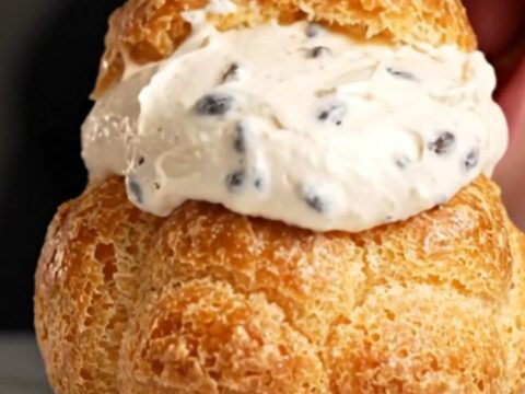 A close-up shot of a golden choux au craquelin puff with a shattered cookie top, revealing a creamy vanilla filling inside.