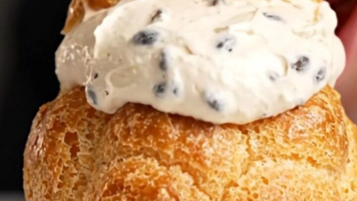 A close-up shot of a golden choux au craquelin puff with a shattered cookie top, revealing a creamy vanilla filling inside.