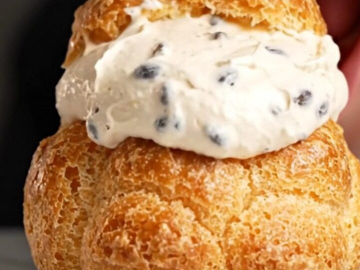 A close-up shot of a golden choux au craquelin puff with a shattered cookie top, revealing a creamy vanilla filling inside.