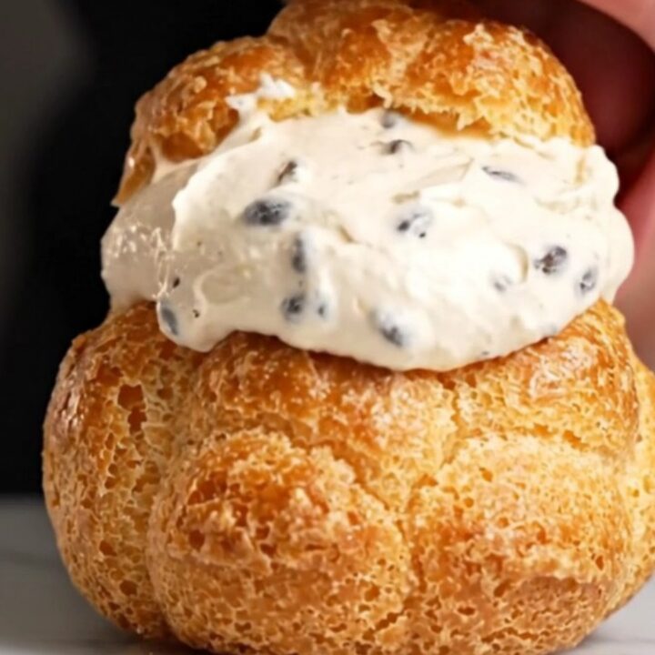 A close-up shot of a golden choux au craquelin puff with a shattered cookie top, revealing a creamy vanilla filling inside.