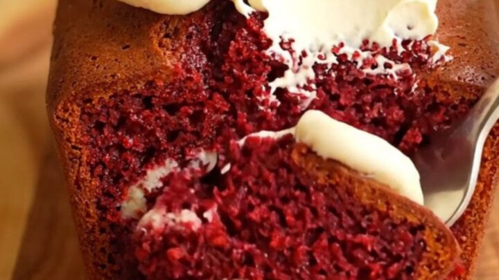 A moist red velvet loaf cake with a cream cheese swirl, topped with thick vanilla frosting and cake crumbs.