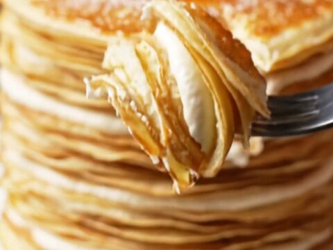A slice of 20-layer mille crêpe cake showing distinct, thin layers with cream and a golden, torched sugar top.