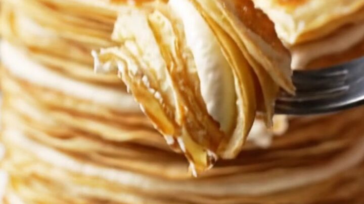 A slice of 20-layer mille crêpe cake showing distinct, thin layers with cream and a golden, torched sugar top.