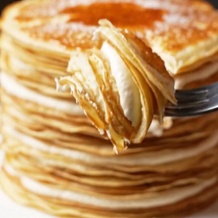 A slice of 20-layer mille crêpe cake showing distinct, thin layers with cream and a golden, torched sugar top.