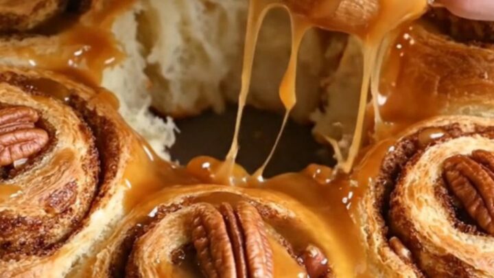 Sticky pecan pie upside-down cinnamon rolls displayed on a platter with amber caramel dripping down the sides.