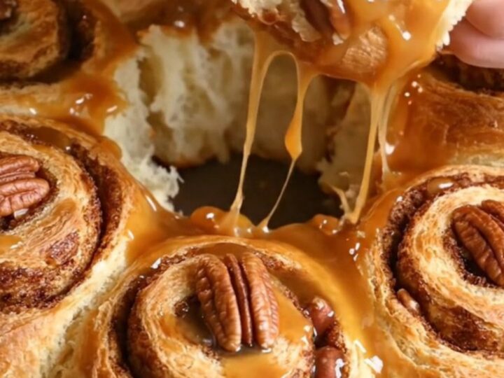 Sticky pecan pie upside-down cinnamon rolls displayed on a platter with amber caramel dripping down the sides.