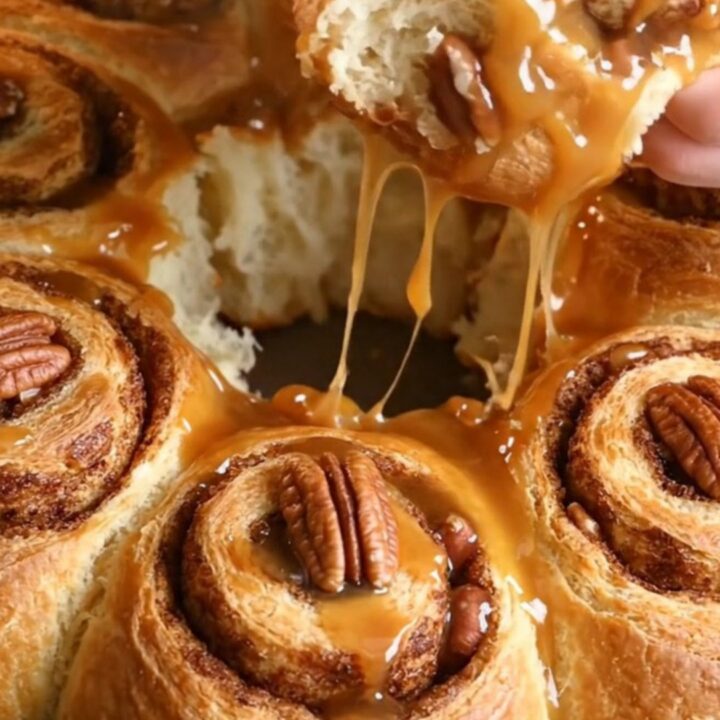 Sticky pecan pie upside-down cinnamon rolls displayed on a platter with amber caramel dripping down the sides.