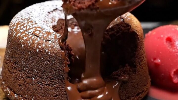 A warm, decadent molten dark chocolate lava cake on a slate plate with a river of chocolate flowing out.