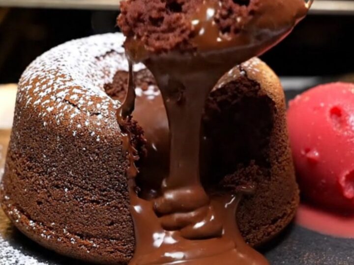 A warm, decadent molten dark chocolate lava cake on a slate plate with a river of chocolate flowing out.