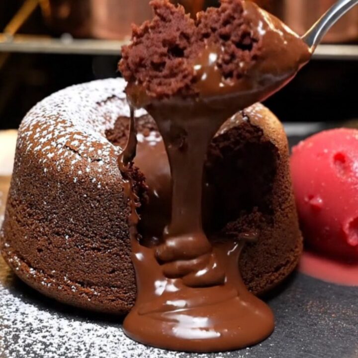 A warm, decadent molten dark chocolate lava cake on a slate plate with a river of chocolate flowing out.