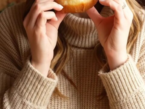 A warm, freshly fried apple cider doughnut being broken in half, revealing a tender golden spiced crumb.