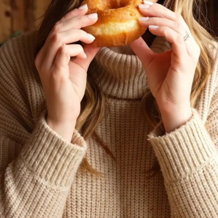 A warm, freshly fried apple cider doughnut being broken in half, revealing a tender golden spiced crumb.