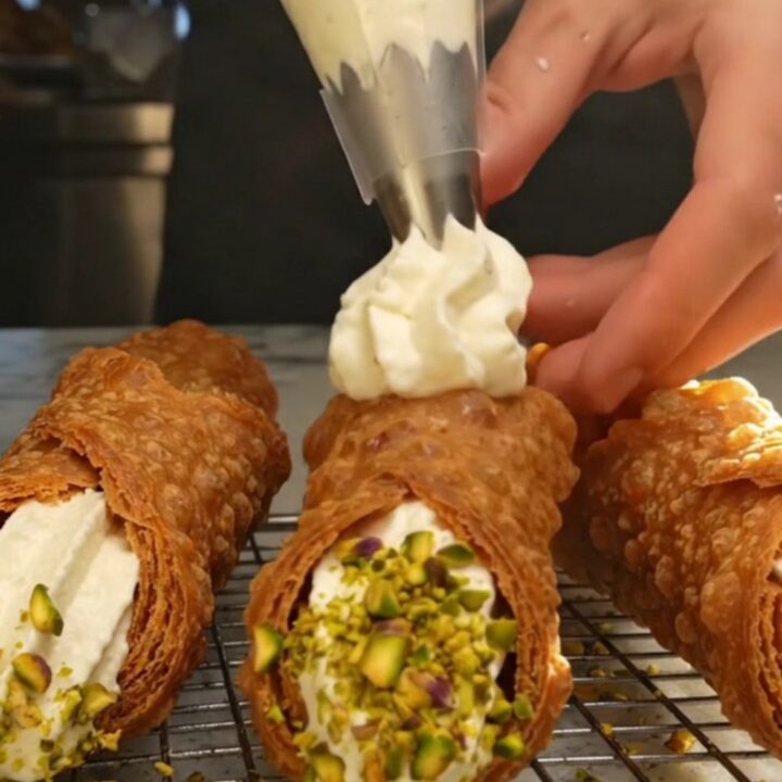 A close-up of a freshly filled Sicilian cannoli with a golden, blistered shell and crushed pistachios on the ends.
