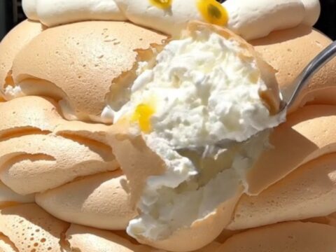A tall, elegant passionfruit pavlova with a crisp white meringue shell topped with whipped cream and fruit.