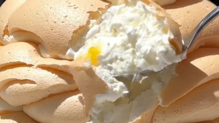 A tall, elegant passionfruit pavlova with a crisp white meringue shell topped with whipped cream and fruit.