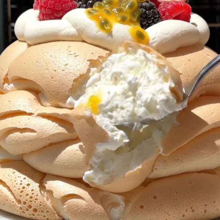 A tall, elegant passionfruit pavlova with a crisp white meringue shell topped with whipped cream and fruit.