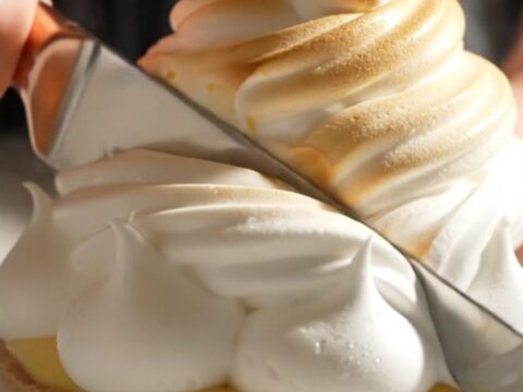 A close-up of a lemon meringue tart with perfectly torched peaks and a slice removed.