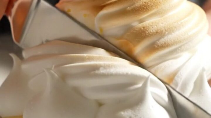 A close-up of a lemon meringue tart with perfectly torched peaks and a slice removed.