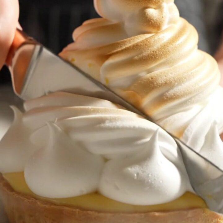 A close-up of a lemon meringue tart with perfectly torched peaks and a slice removed.