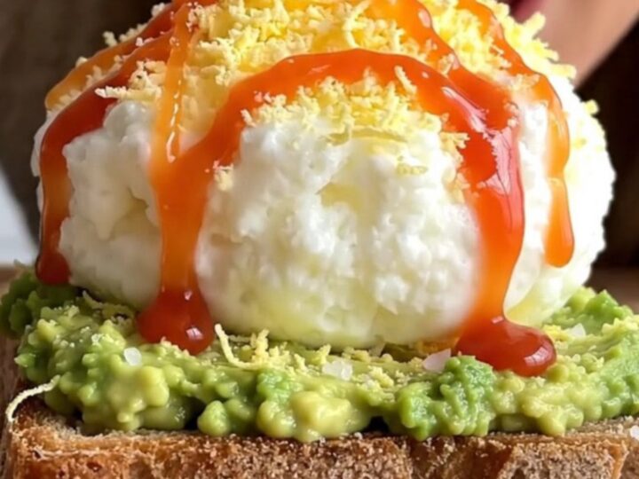 A close-up of two pieces of sourdough toast topped with creamy avocado and a light layer of grated hard-boiled egg.