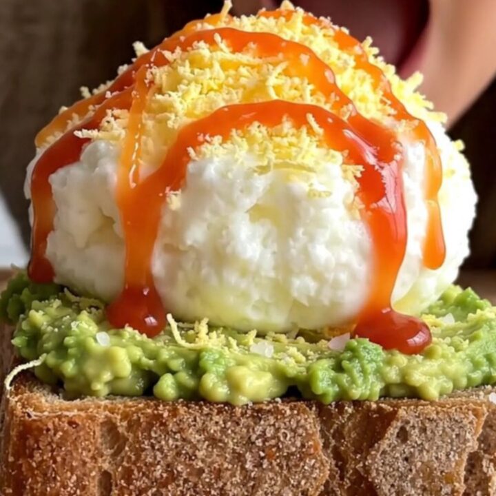 A close-up of two pieces of sourdough toast topped with creamy avocado and a light layer of grated hard-boiled egg.