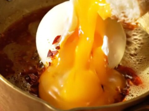 A close-up of two poached eggs resting on a bed of garlic yogurt, drizzled with bright red Aleppo chili butter.