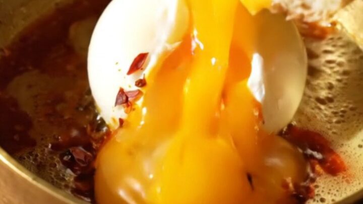 A close-up of two poached eggs resting on a bed of garlic yogurt, drizzled with bright red Aleppo chili butter.