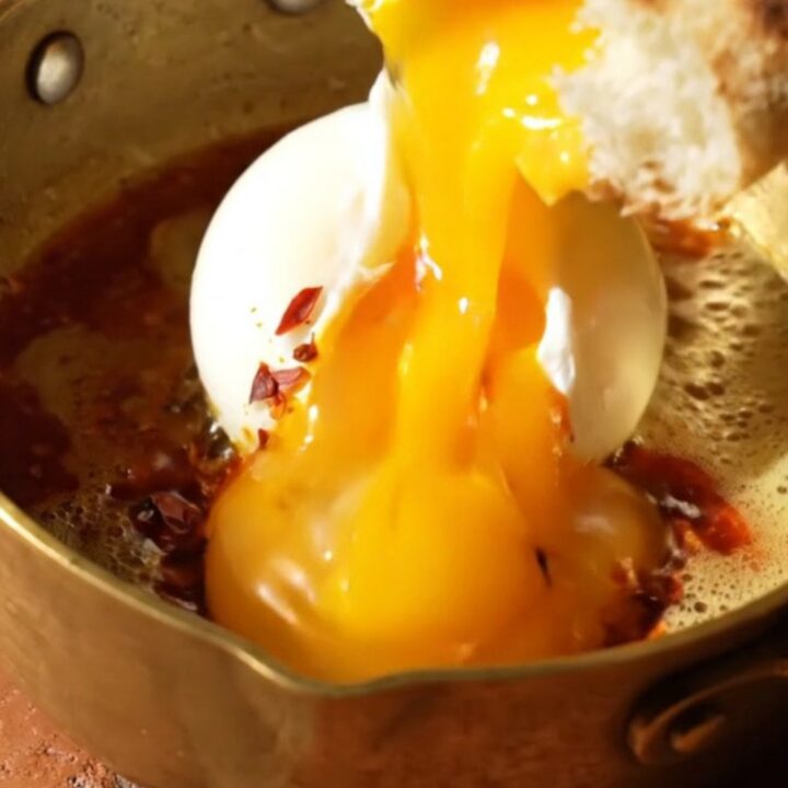 A close-up of two poached eggs resting on a bed of garlic yogurt, drizzled with bright red Aleppo chili butter.