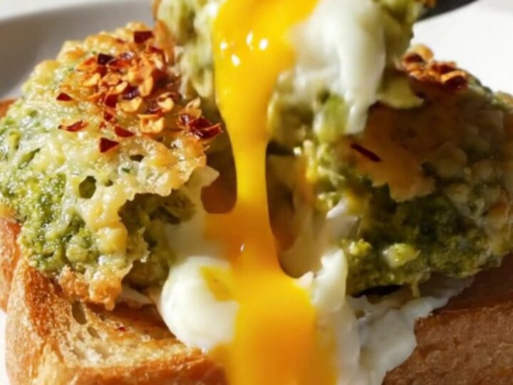 A close-up of two sunny-side-up eggs with a crispy Parmesan lace and green pesto, resting on a slice of toasted brioche.