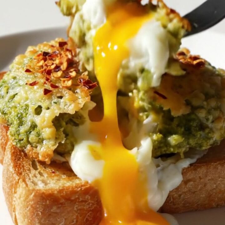 A close-up of two sunny-side-up eggs with a crispy Parmesan lace and green pesto, resting on a slice of toasted brioche.