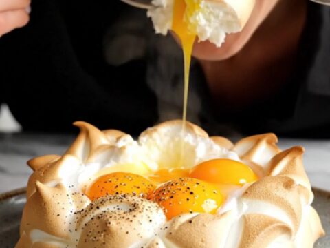 A macro shot of a golden egg yolk centered in a pillowy, toasted meringue cloud with herbs.