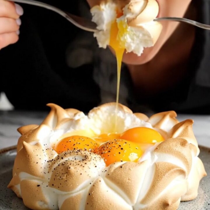 A macro shot of a golden egg yolk centered in a pillowy, toasted meringue cloud with herbs.