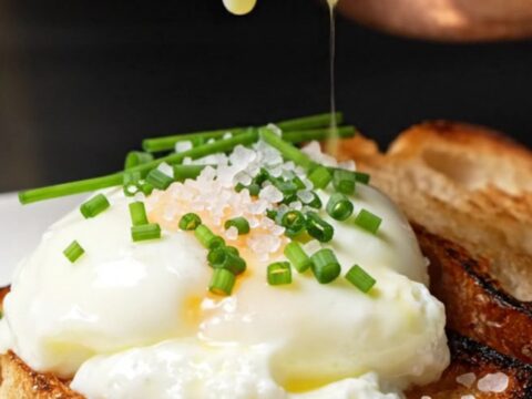 Glossy, soft-curd scrambled eggs served on a piece of charred brioche toast, garnished with chives.