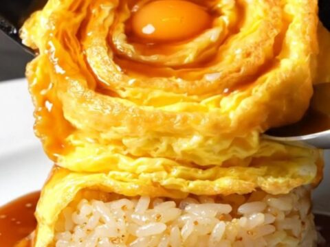 A perfectly formed golden tornado omelette draped over a bed of glossy garlic butter rice, topped with demi-glace.