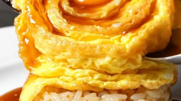 A perfectly formed golden tornado omelette draped over a bed of glossy garlic butter rice, topped with demi-glace.