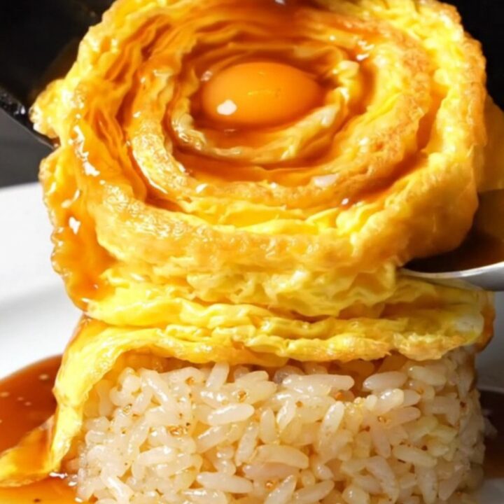 A perfectly formed golden tornado omelette draped over a bed of glossy garlic butter rice, topped with demi-glace.