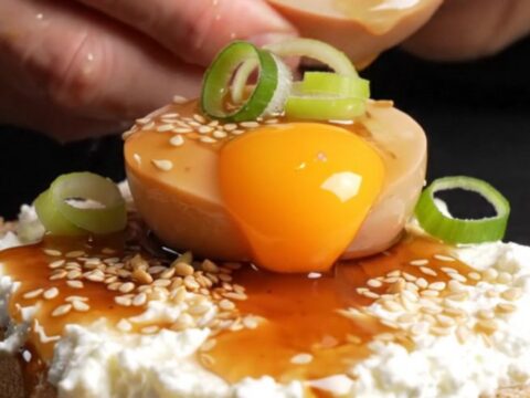 A close-up shot of a jammy soy-marinated egg sliced in half, revealing a translucent amber yolk on toasted sourdough bread.