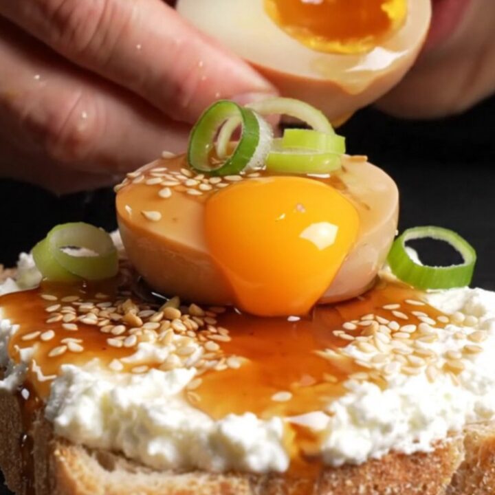 A close-up shot of a jammy soy-marinated egg sliced in half, revealing a translucent amber yolk on toasted sourdough bread.
