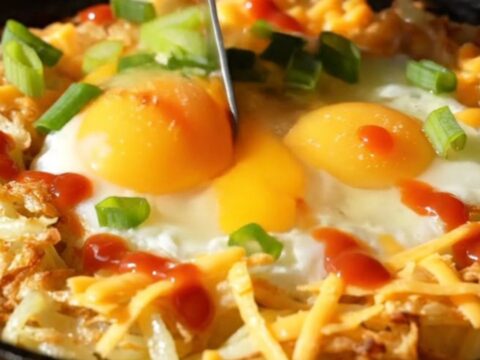 A golden-brown shredded potato nest in a cast-iron skillet, filled with two perfectly baked eggs and melted sharp cheddar.