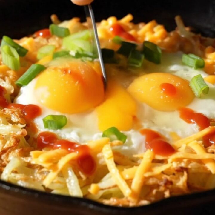 A golden-brown shredded potato nest in a cast-iron skillet, filled with two perfectly baked eggs and melted sharp cheddar.